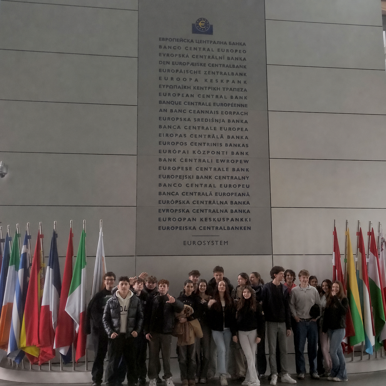 Gruppe junger Menschen steht vor einer Wand mit der mehrsprachigen Aufschrift "Europäische Zentralbank" und mehreren Flaggen europäischer Länder. mit KI bearbeitet loading=