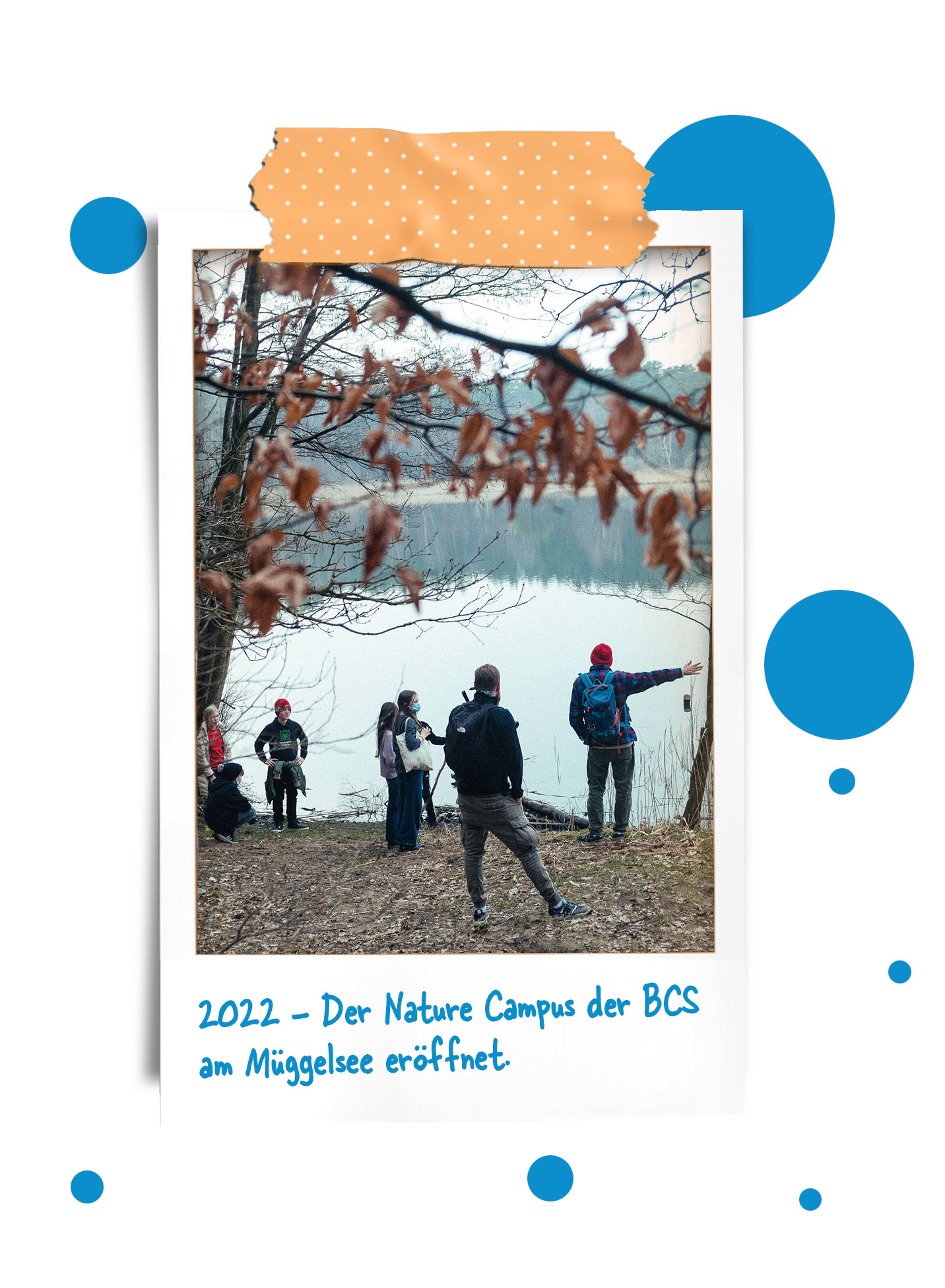 Cosmopolitanschool Berlin Eine Gruppe von Menschen steht am Ufer des Müggelsees, umgeben von Bäumen mit Herbstlaub. Eine Person zeigt auf das Wasser. Der Text darunter lautet: 2022 - Der Nature Campus der BCS am Müggelsee eröffnet. loading=