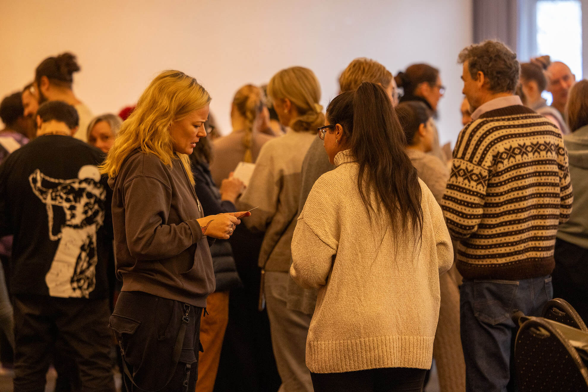 Cosmopolitanschool Berlin Eine Gruppe von Menschen steht dicht beieinander in einem Raum und unterhält sich in kleinen Gruppen. Die meisten sind leger und warm gekleidet. Im Vordergrund stehen sich zwei Frauen - eine davon möglicherweise Karth Murdoch - gegenüber und scheinen ein Gespräch zu führen.