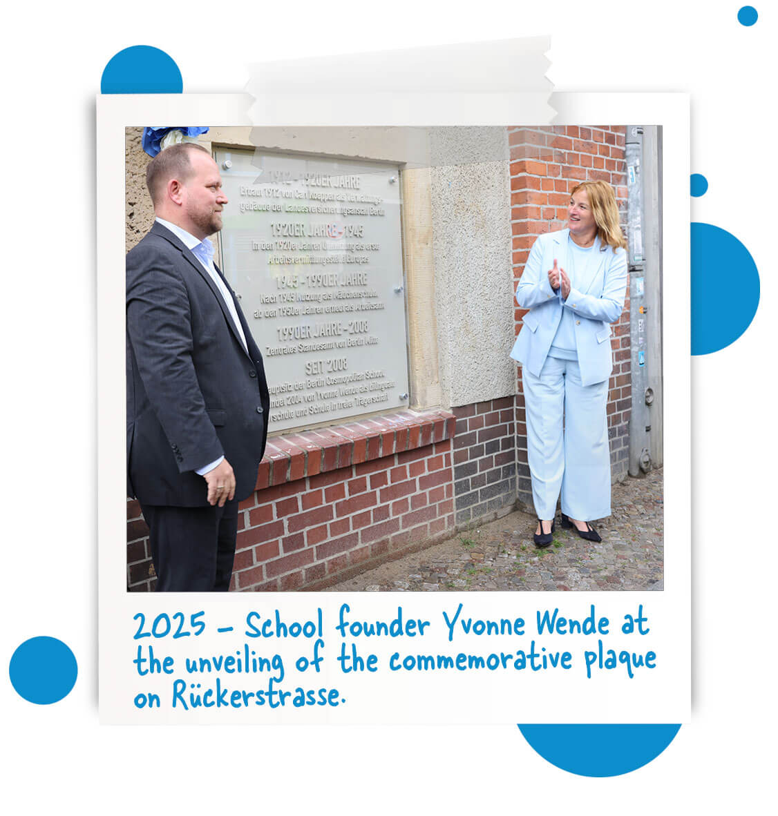 Cosmopolitanschool Berlin Zwei Personen stehen neben einer an der Wand befestigten Gedenktafel. Die Frau auf der rechten Seite klatscht lächelnd, während der Mann auf der linken Seite sie anschaut. Im Text darunter steht, dass es sich um die Enthüllung durch die Schulgründerin Yvonne Wende im Jahr 2025 handelt. loading=