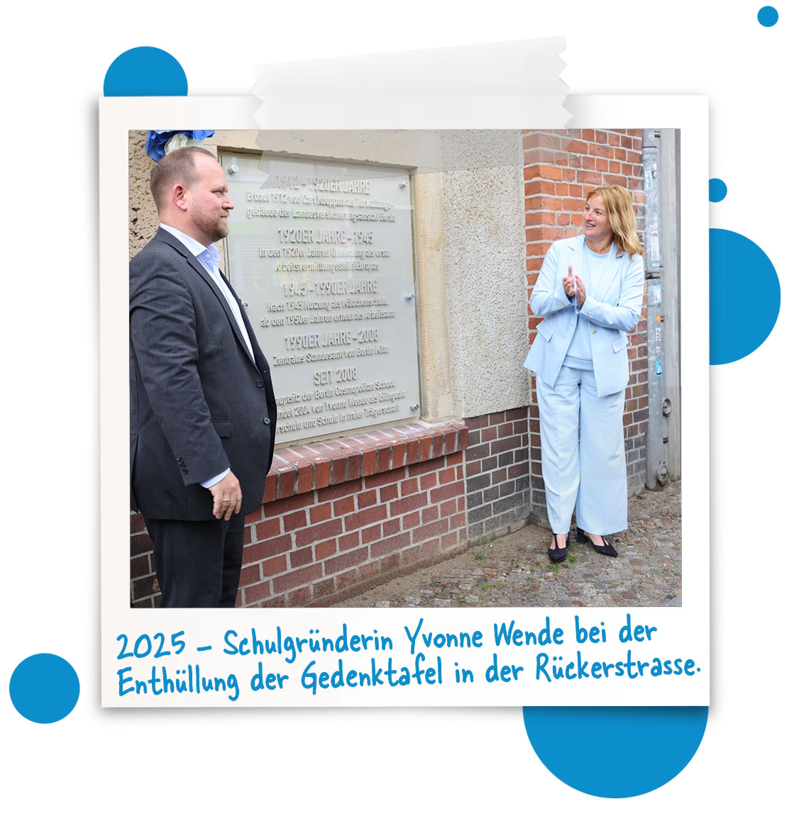Cosmopolitanschool Berlin Ein Mann und eine Frau in formeller Kleidung stehen neben einer Gedenktafel an einer Backsteinmauer. Die Frau klatscht, während der Mann in Richtung der Gedenktafel gestikuliert. Der folgende deutsche Text beschreibt die Enthüllung im Jahr 2025. loading=