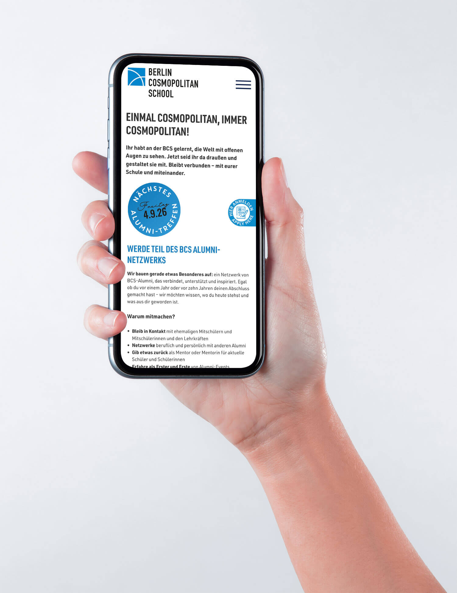 Cosmopolitanschool Berlin Eine Hand hält ein Smartphone, auf dem die BCS Alumni-Website der Berlin Cosmopolitan School mit deutschem Text und einem blauen, kreisförmigen Alumni-Netzwerk-Badge angezeigt wird. loading=