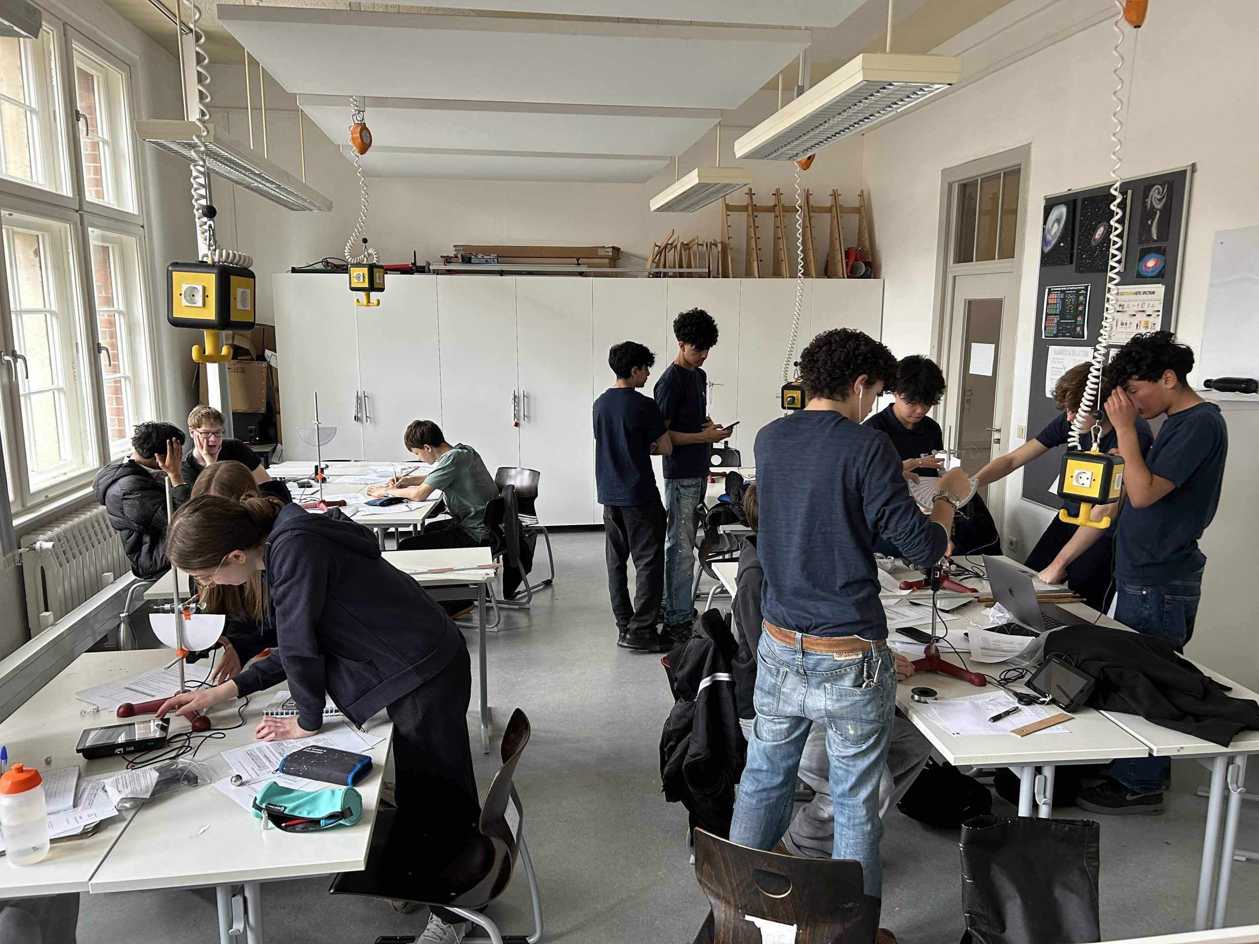 Cosmopolitanschool Berlin Ein Klassenzimmer mit Schülern, die in Gruppen an Labortischen an wissenschaftlichen Experimenten arbeiten. Laborgeräte und Papiere sind ausgebreitet, und einige Schüler schreiben oder diskutieren, während andere die Geräte einstellen. loading=