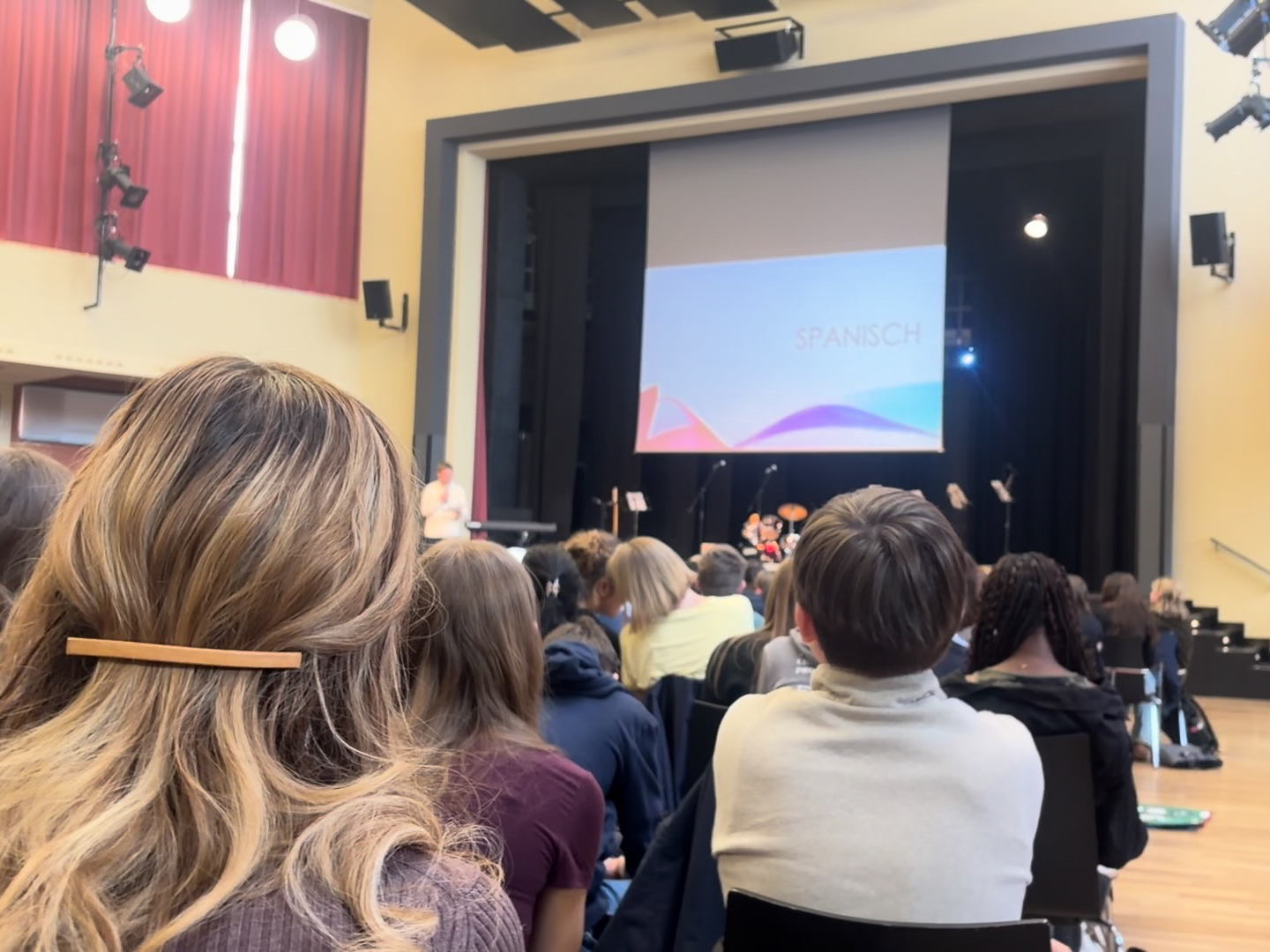Publikum von hinten in einem Saal mit Bühne und Leinwand, auf der eine Präsentation läuft loading=