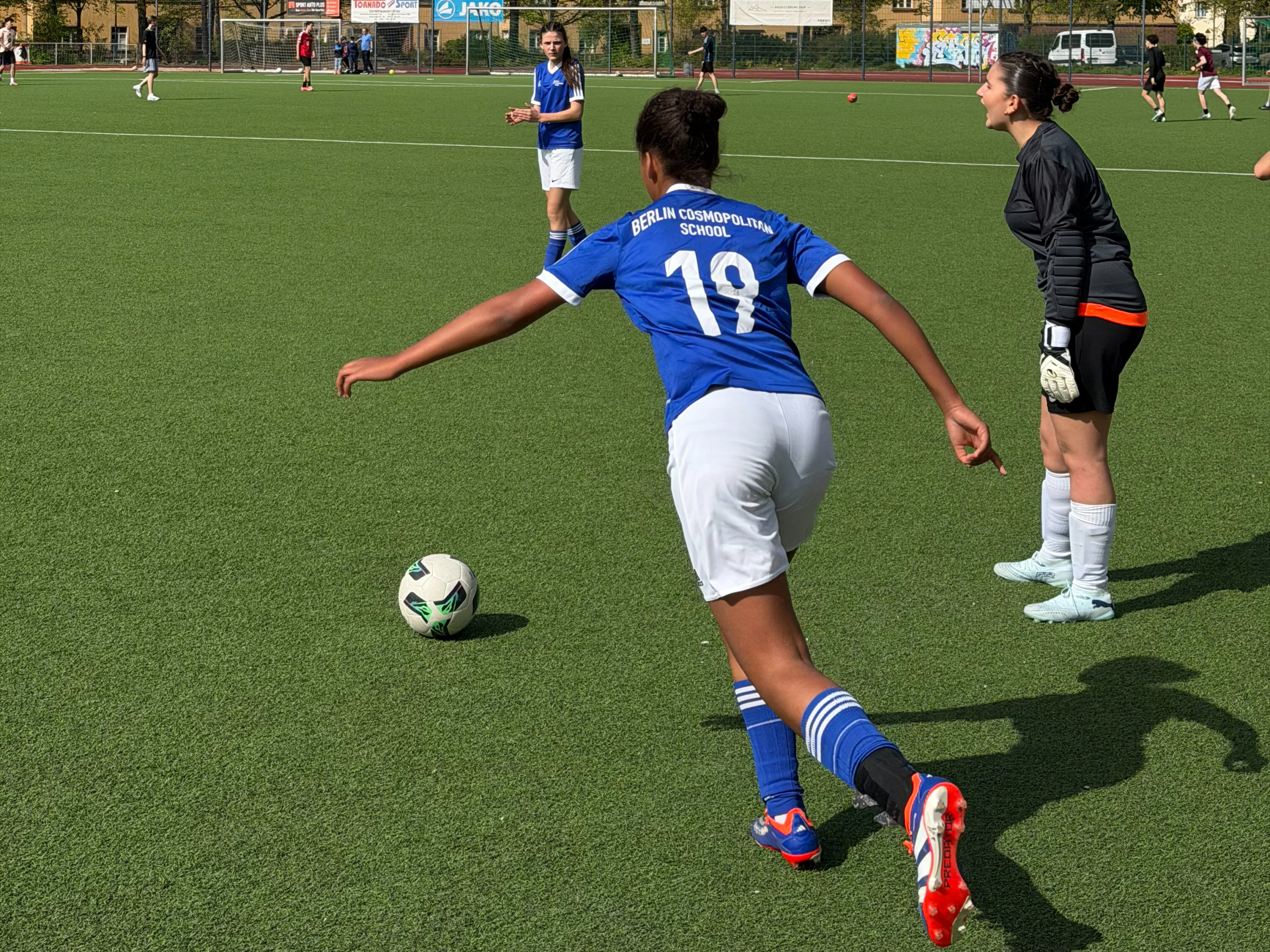 Cosmopolitanschool Berlin Fußballspielerin der Cosmopolitanschool Berlin mit Trikotnummer 19 beim Schuss auf den Ball vor der Torhüterin auf dem Spielfeld loading=