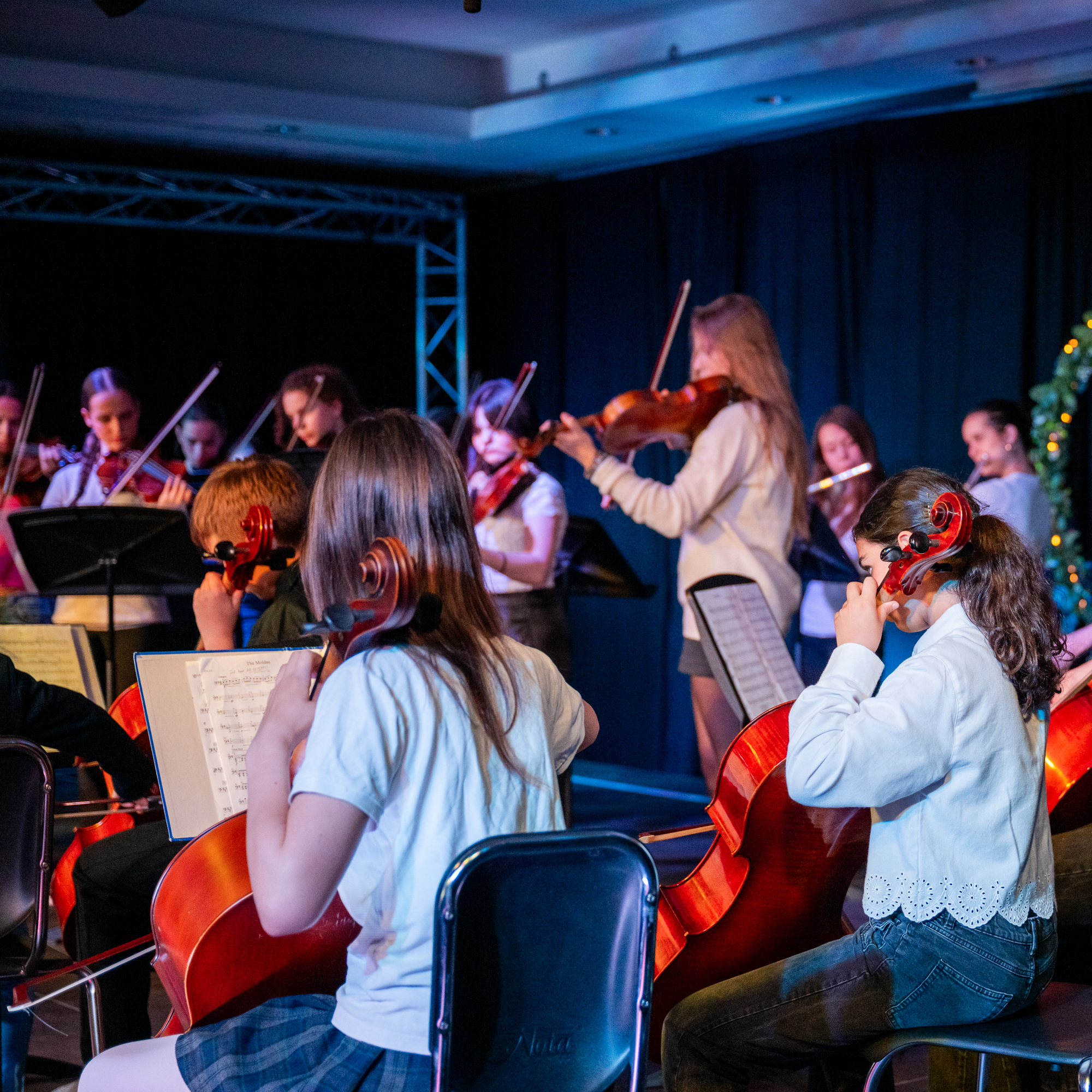 Kinder spielen in einem Orchester auf Stühlen sitzend Cello und Geige loading=