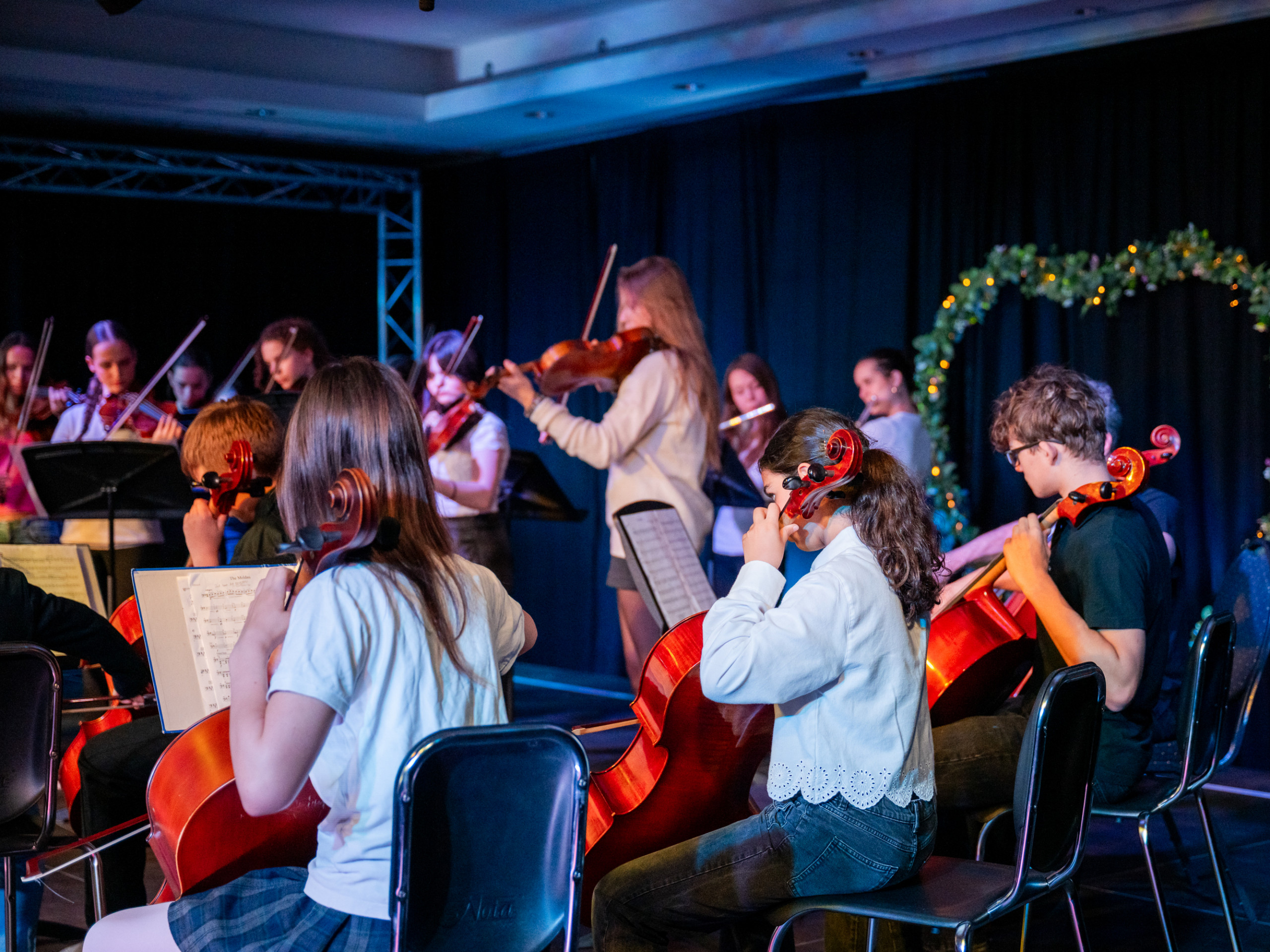 Kinder spielen in einem Orchester verschiedene Streichinstrumente wie Cello und Geige auf einer Bühne loading=