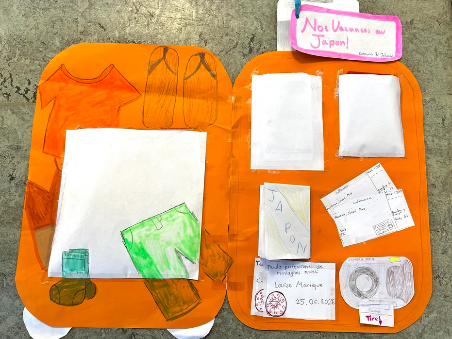 Aufgeschlagene orangefarbene Bastelmappe mit gezeichneten Kleidungsstücken und mehreren weißen Papierstücken, darunter ein Brief mit dem Wort 'JAPON' und ein handgeschriebener Zettel mit 'Nos Vacances au Japon' loading=